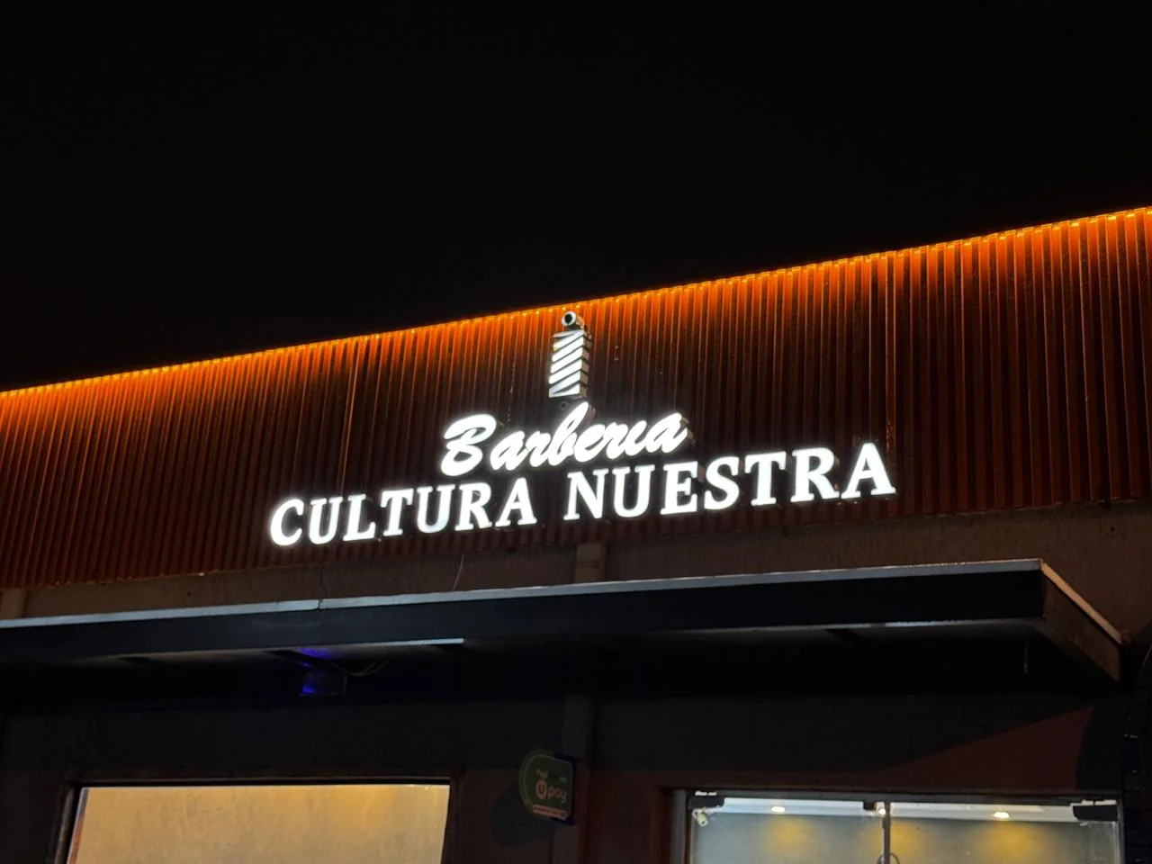 Fachada nocturna iluminada de Barbería Cultura Nuestra